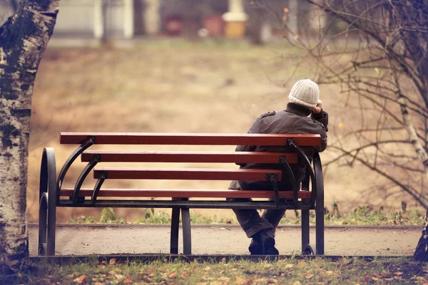 Одинокий человек на скамейке осенью — стоковое фото