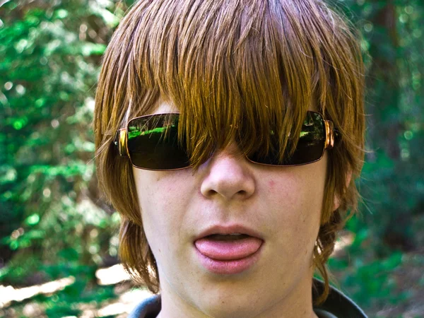 Мальчик с красным длинные волосы и солнцезащитные очки pocks его язык и выглядит реальным — стоковое фото