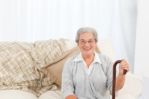 Зрелая женщина, сидя на диване с ее трость — стоковое фото